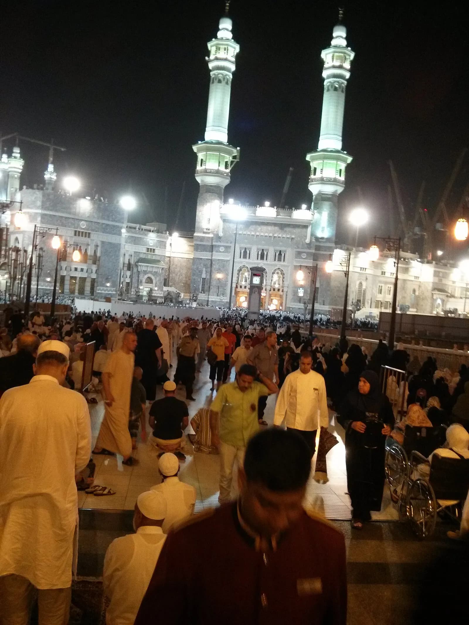 Pilgrims walking beneath the minarets of Masjid al-Haram at night